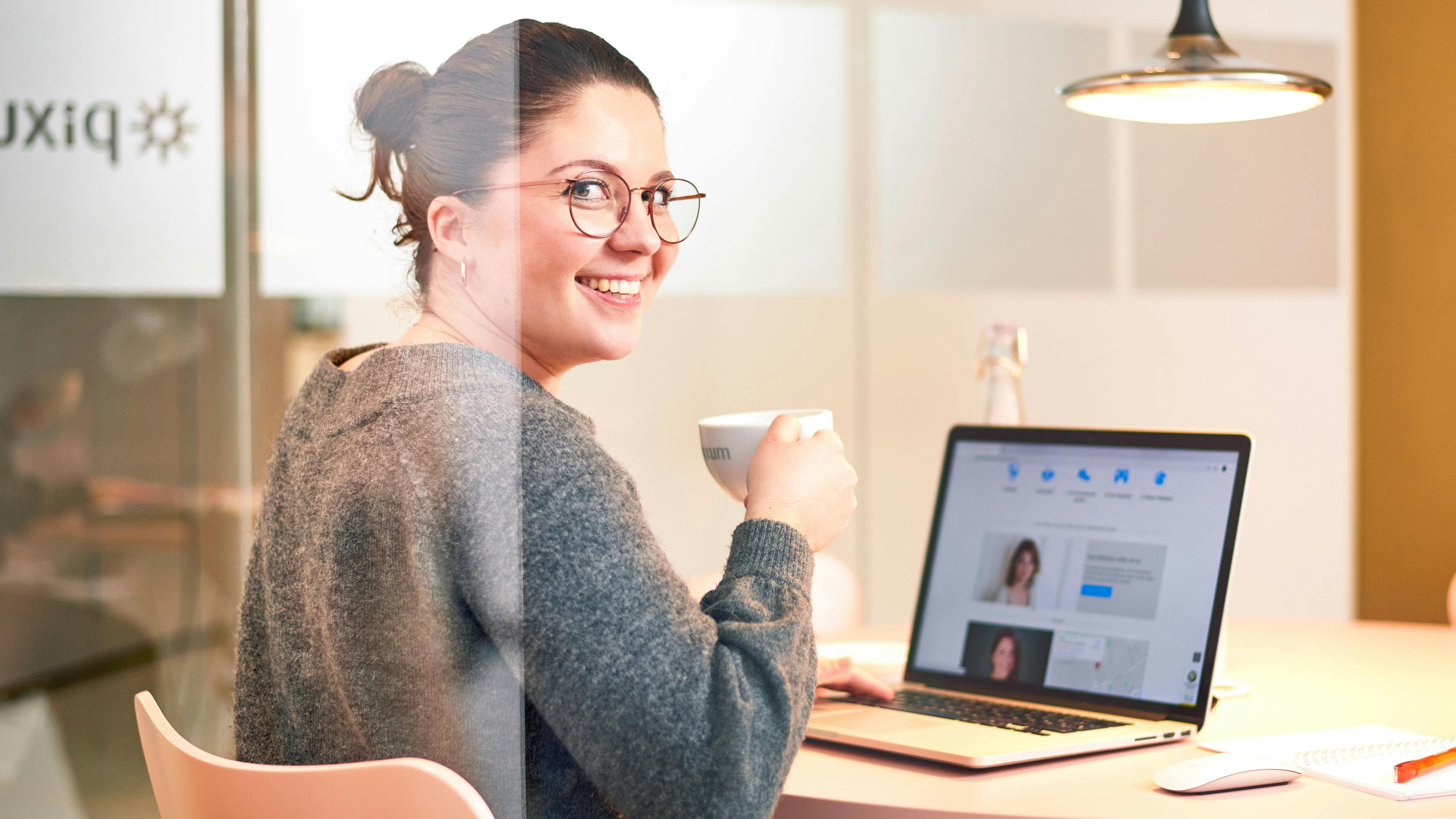 img_unternehmen_bewerbungsratgeber_ncu-bewerbung-laptop Mitarbeiterin sitzt mit einem Kaffee vor einem Laptop