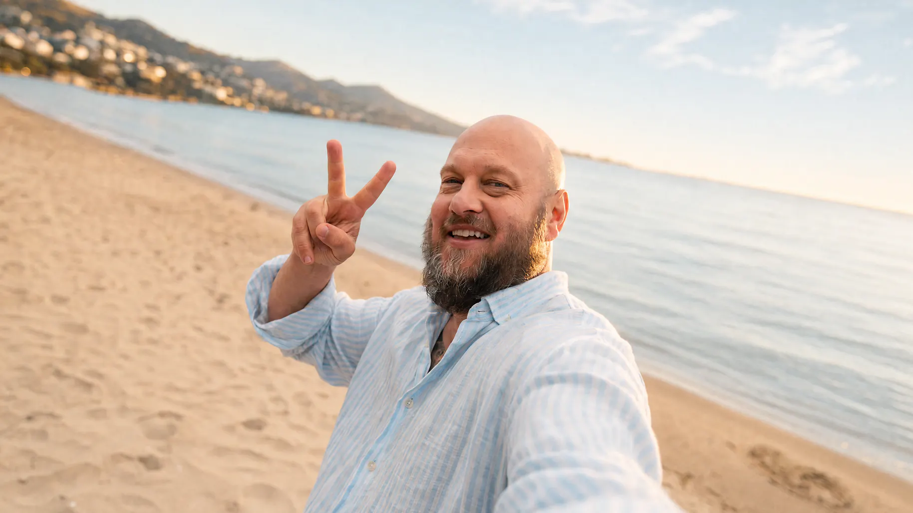 Ein Mann mit Glatze am Strand zeigt mit seinen Händen ein Peace-Zeichen