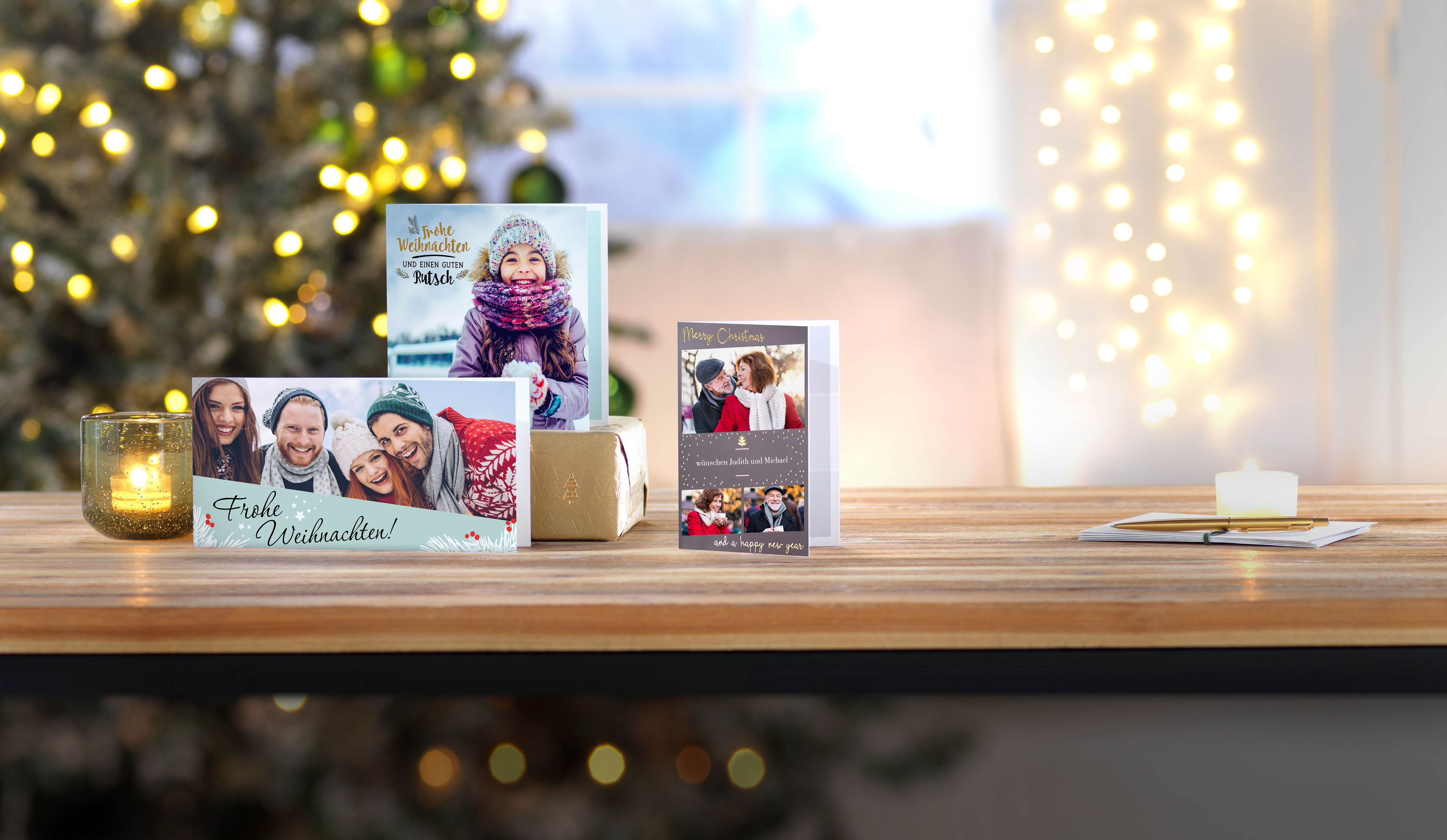 Een selectie van drie gevouwen, gepersonaliseerde wenskaarten met kerstgroeten en foto's van een ouder echtpaar, een groep vrienden en een gelukkig meisje, op een tafel voor een kerstboom.