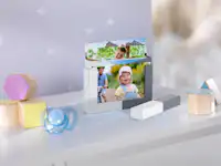 Pixum Fotobox mit Rahmen Eine Fotobox mit Rahmen ist mit verschiedenen Fotoabzügen von einer Familie mit Baby befüllt