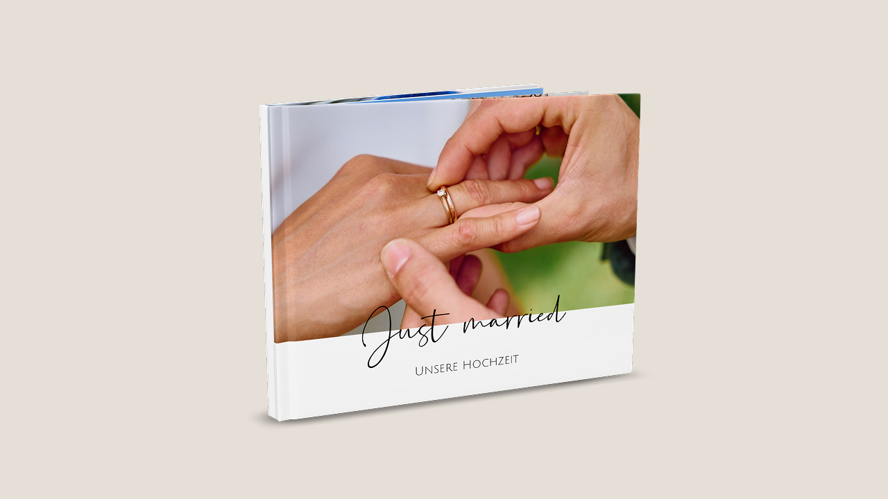 Ein aufgestelltes Fotobuch zeigt ein Foto von einer Hochzeit. Auf dem Foto werden gerade die Ringe ausgetauscht. Halb über dem Foto ist der Titel "Just married" platziert. Darunter ein zweiter Titel "Unsere Hochzeit"