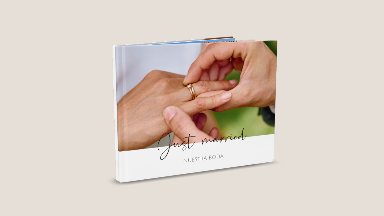 En un álbum de fotos colocado en posición vertical se ve una foto de una boda. En la foto, los novios se están intercambiando los anillos. En la parte superior de la foto aparece el título «Just married». Debajo hay un segundo título: «Nuestra boda».