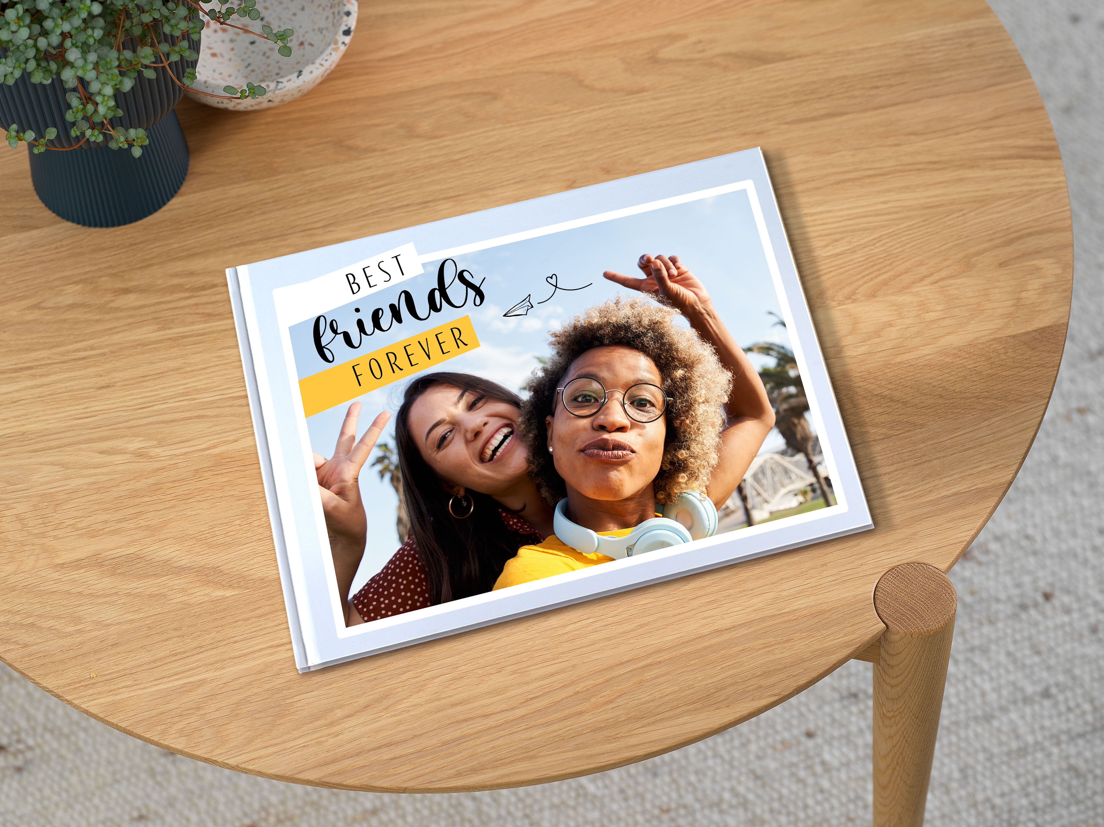 Ein Pixum Fotobuch im großen Hochformat, welches auf einem Tisch liegt. Auf dem Cover steht "Best Friends Forever".