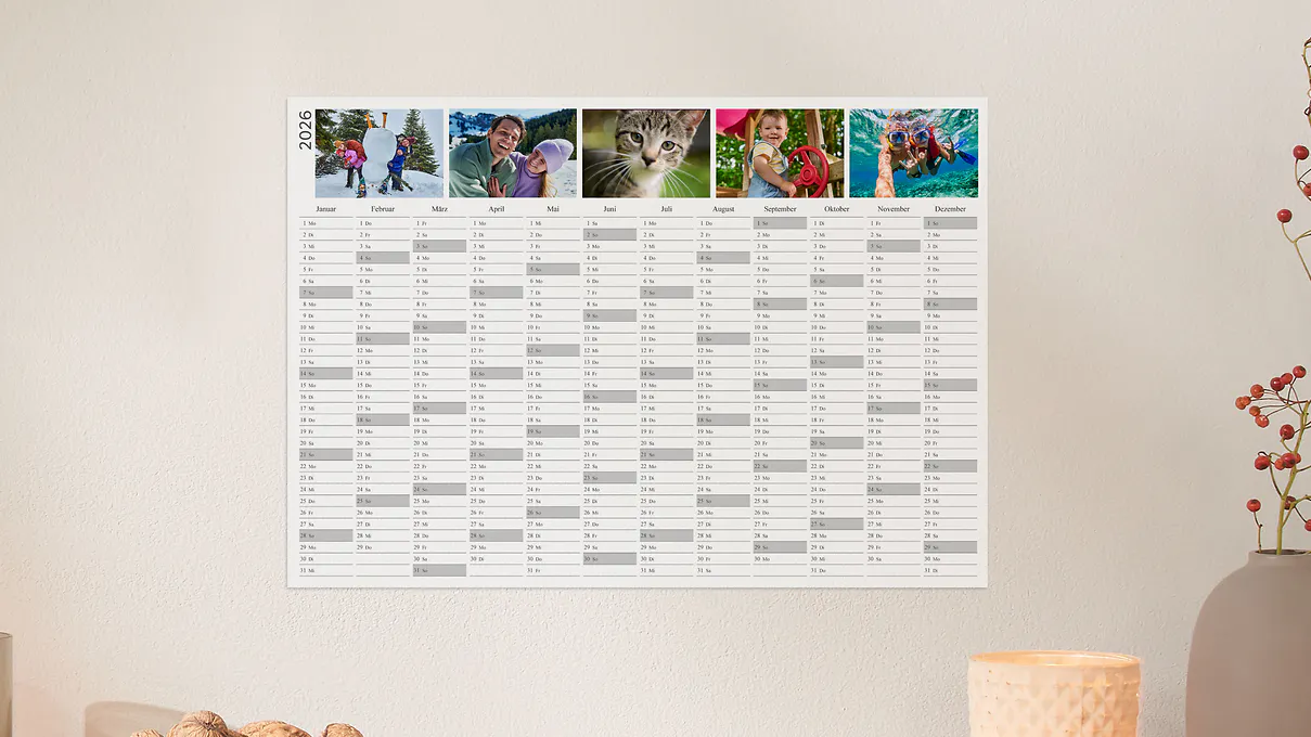 Een jaarplanner in A3-formaat met verschillende foto's hangt aan een muur.