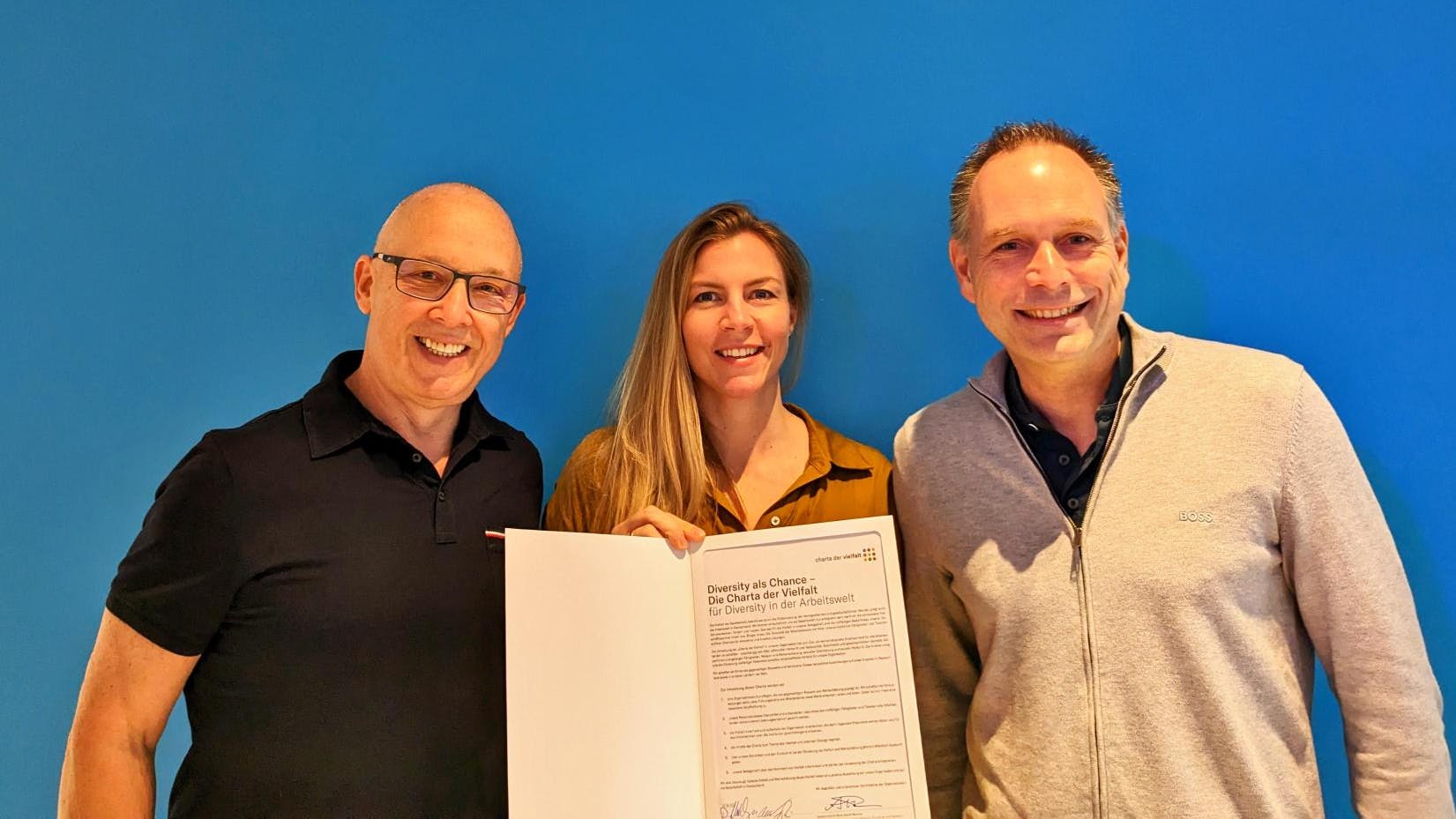 Daniel Attallah, Nora Engels und Marc Rendel mit der unterzeichneten Charta der Vielfalt vor dem Pixum Logo