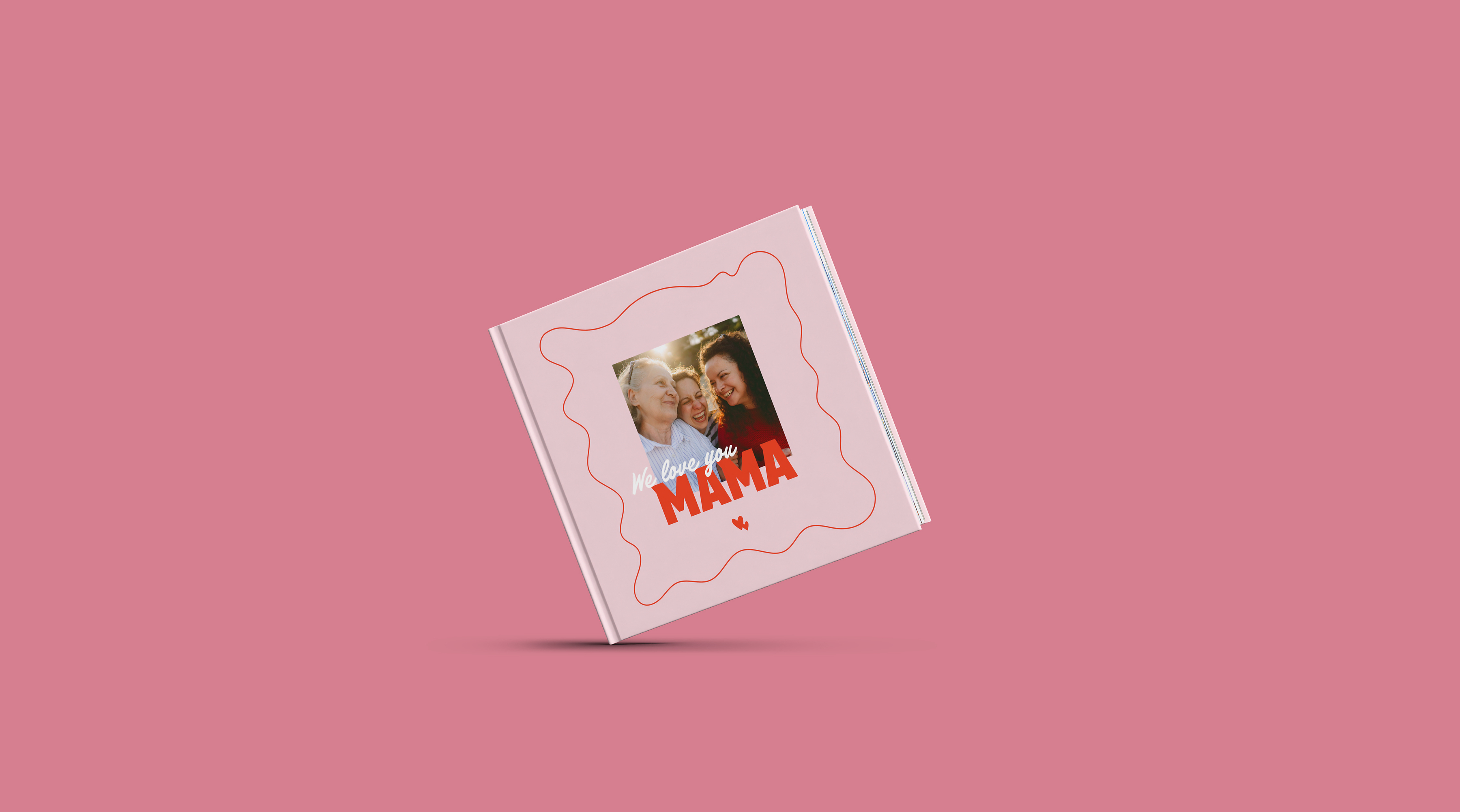 Eine Person hält ein Fotobuch in der Hand. Dieses ist mit rosafarbenen Elementen zum Muttertag gestaltet.