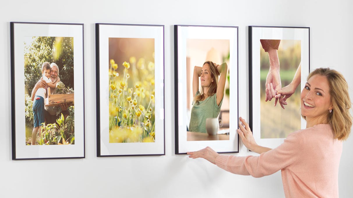 Frau hängt verschiedene gerahmte Bilder an die Wand 