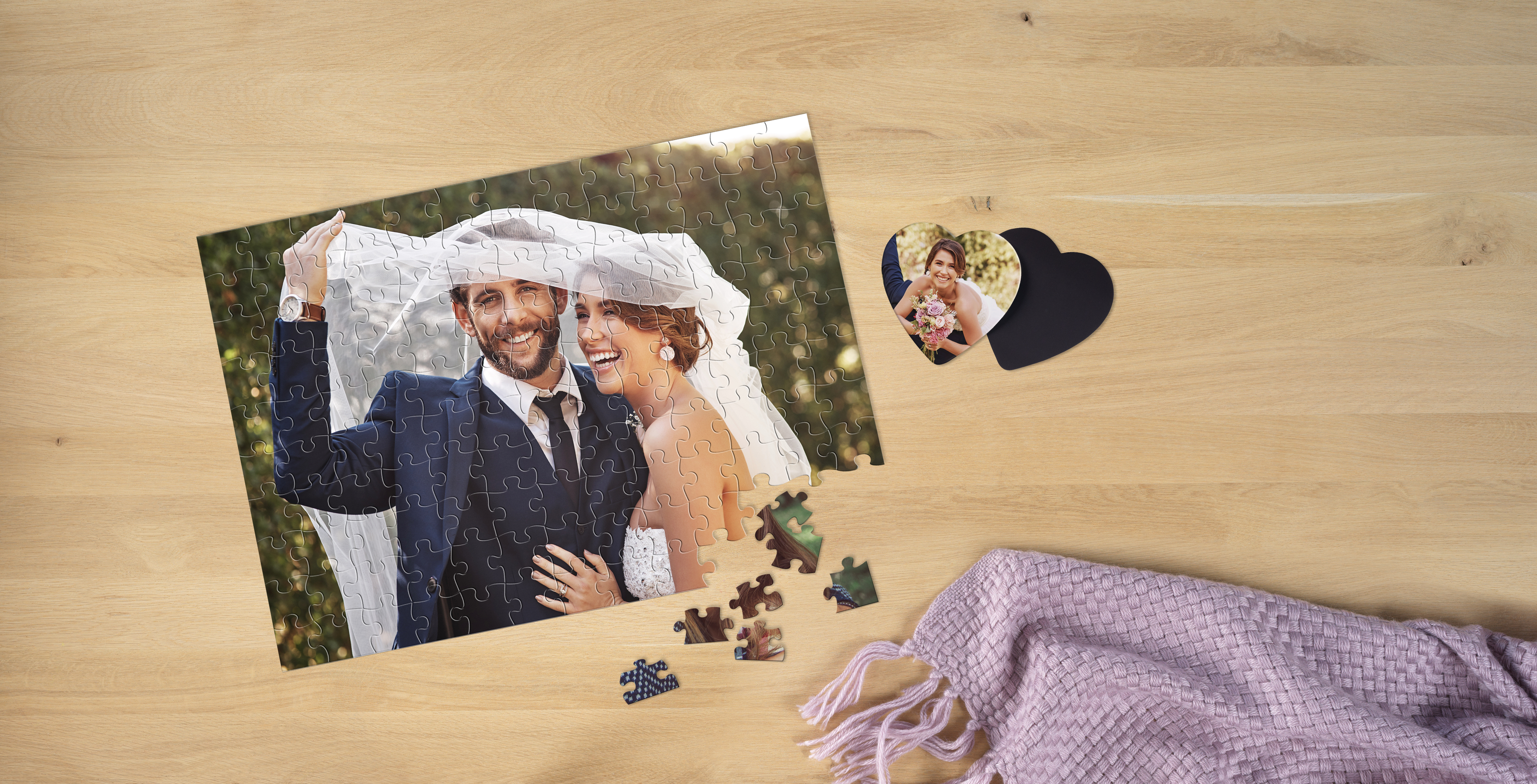 Ein Fotopuzzle zeigt ein lachendes Brautpaar, das sich gemeinsam unter einem Schleier befindet. Daneben liegt ein herzförmiger Fotomagnet der Braut.