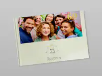 Fotobuch zum 60. Geburtstag Zugeklapptes Fotobuch. Auf dem Cover steht "auf dich Susanne" und die Zahl 60. Es ist ein Foto von einer Familie zu sehen. Darunter ist eine Clipart von zwei anstoßenden Gläsern abgebildet.
