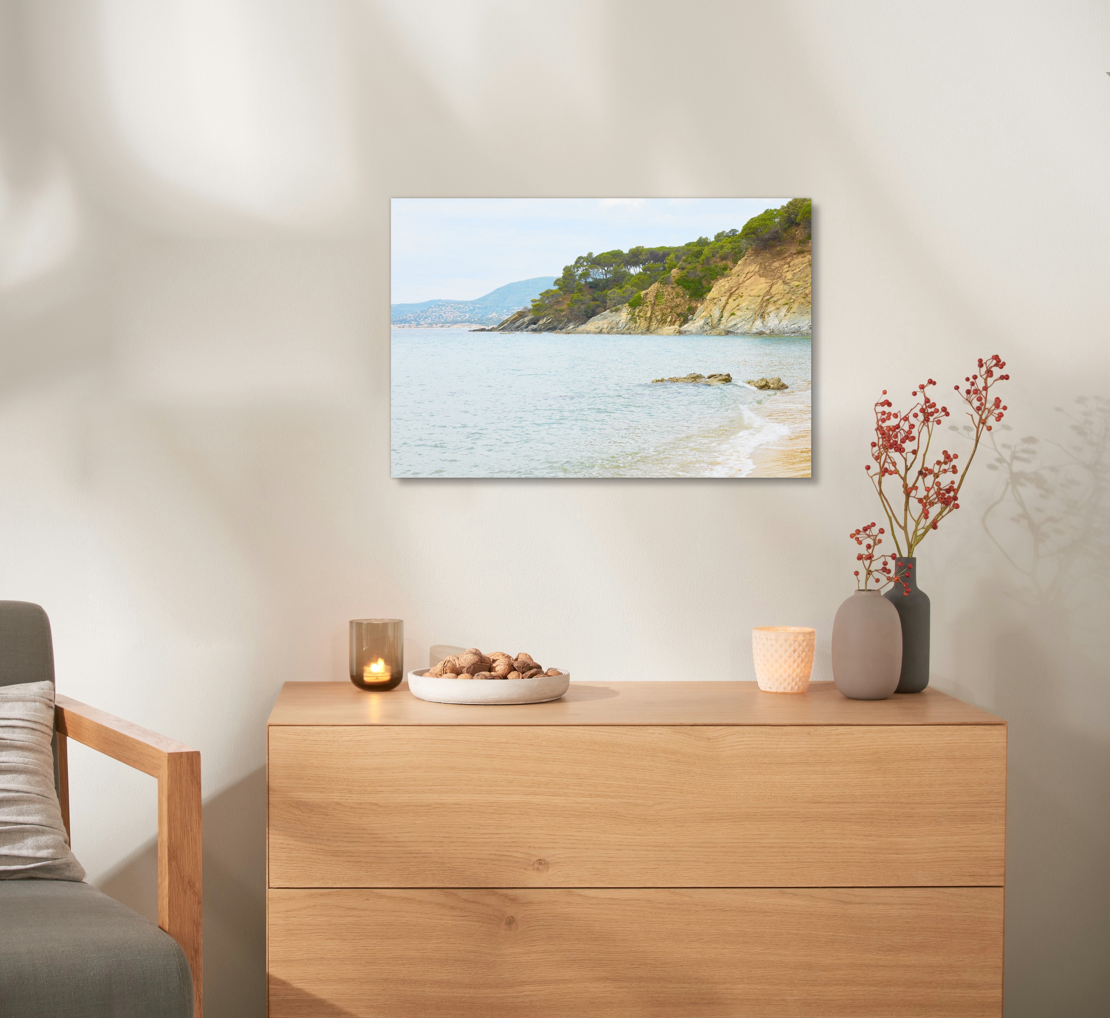 Ein Wandbild aus Holz mit einem Urlaubsfoto hängt an einer Wand, über einer Kommode. 