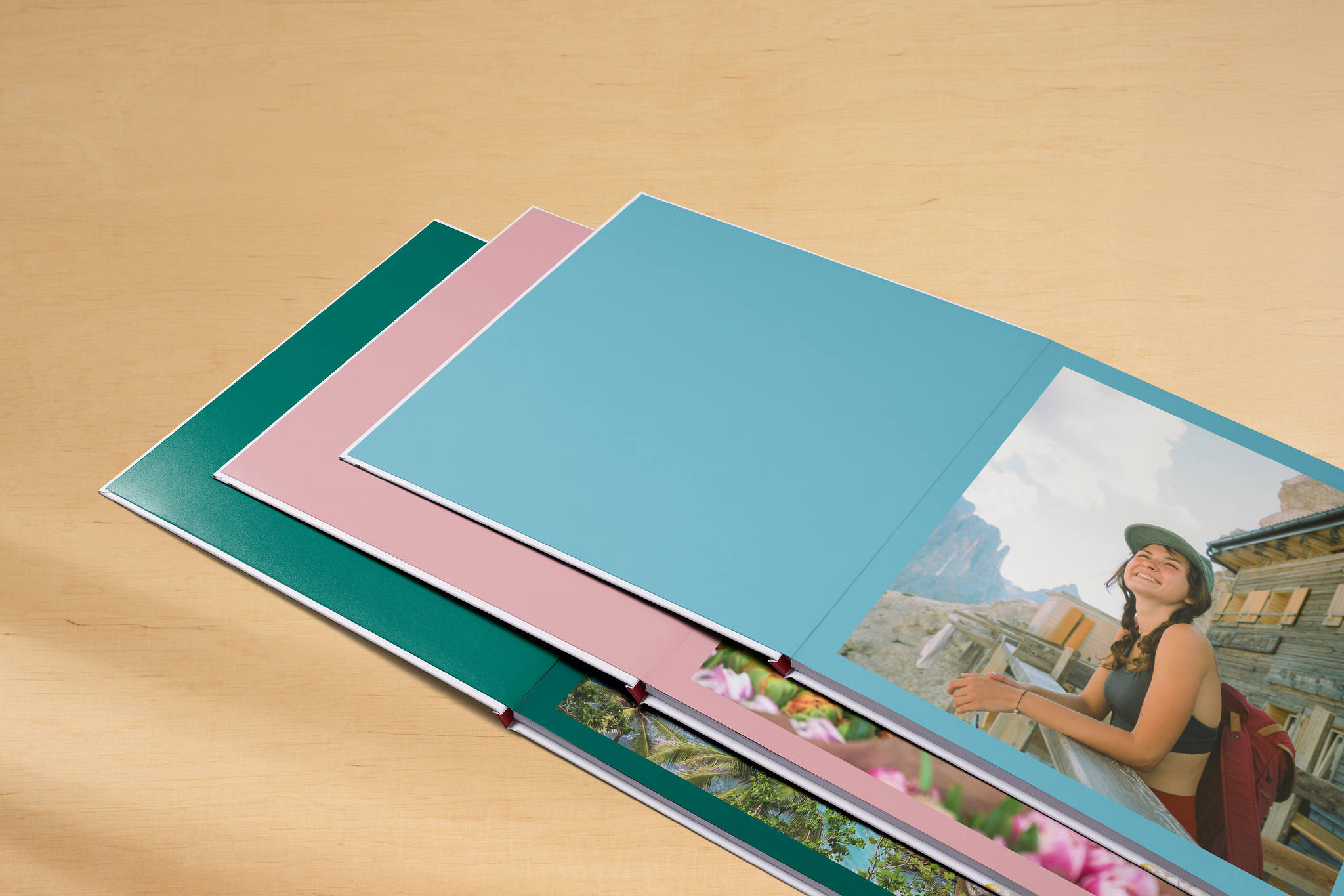 Drei aufgeschlagene Pixum Fotobücher mit farbigen Einband-Innenseiten in Hellblau, Rosa und Grün