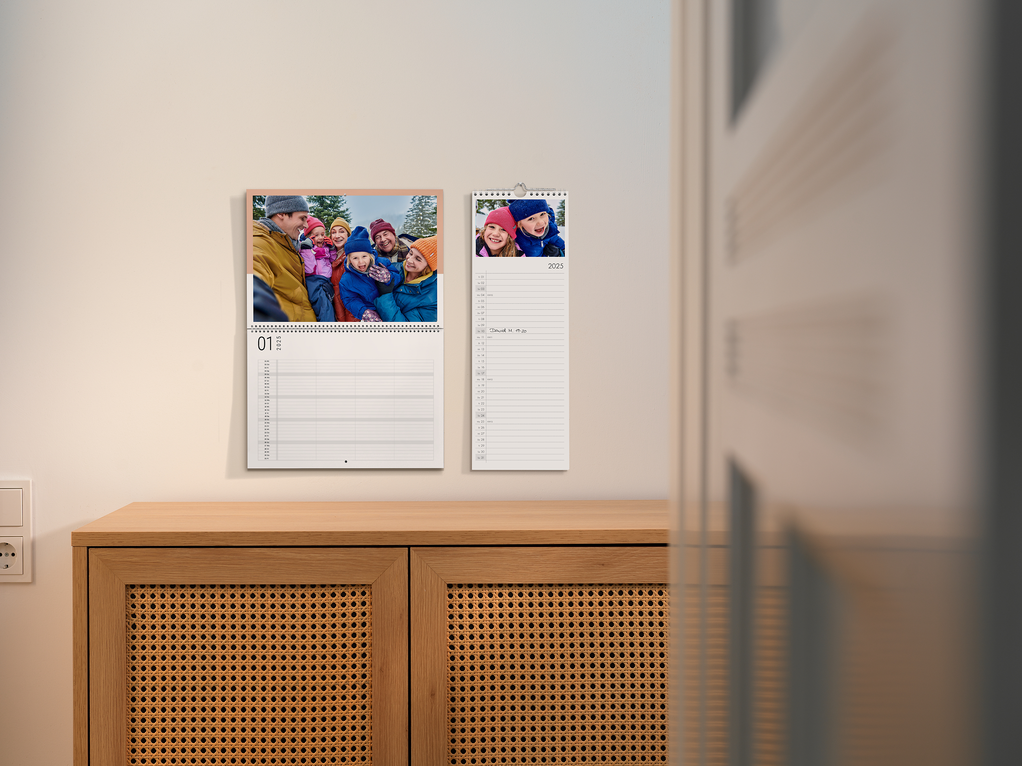 Klappkalender und Küchenkalender mit winterlichen Familienfotos an einer beigen Wand