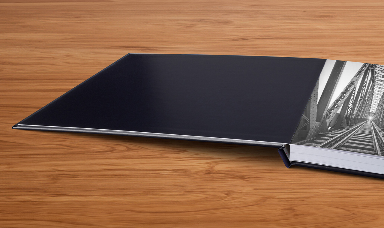 Aufgeklapptes Pixum Fotobuch mit schwarzer Einband-Innenseite auf einem Holztisch liegend