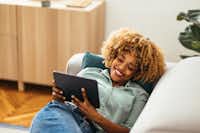 E-Book einfach dazubestellen Eine Frau liegt auf einer Couch, lächelt und schaut sich etwas auf einem Tablet an