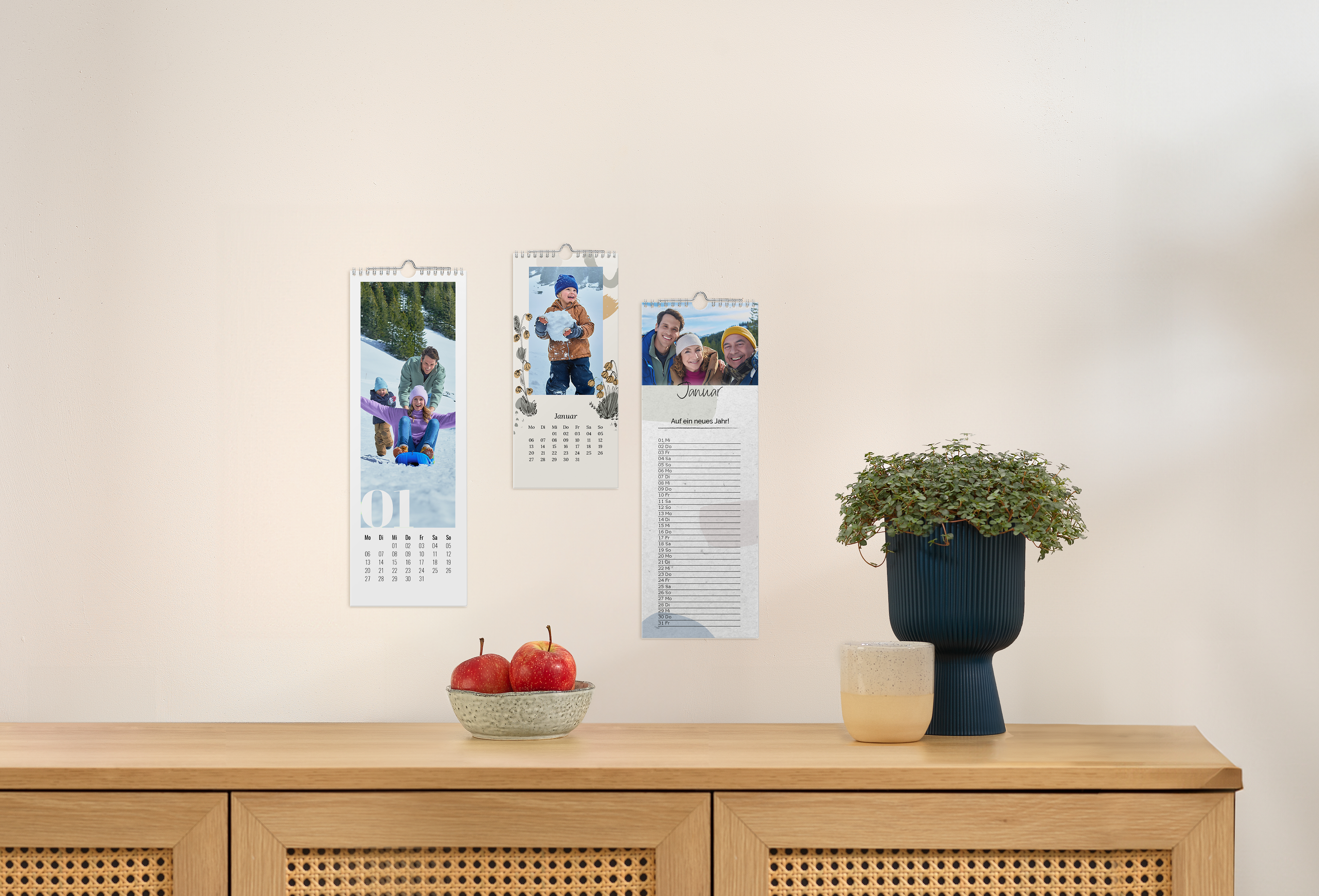 Drei Küchenkalender mit unterschiedlichen Designs und winterlichen Familienbildern an einer Wand