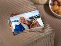 Fotoabzüge von der Familie bestellen Ein Stapel von Fotoabzügen liegt auf einer beigen Couch. Auf den Abzügen sind Familienfotos abgebildet.