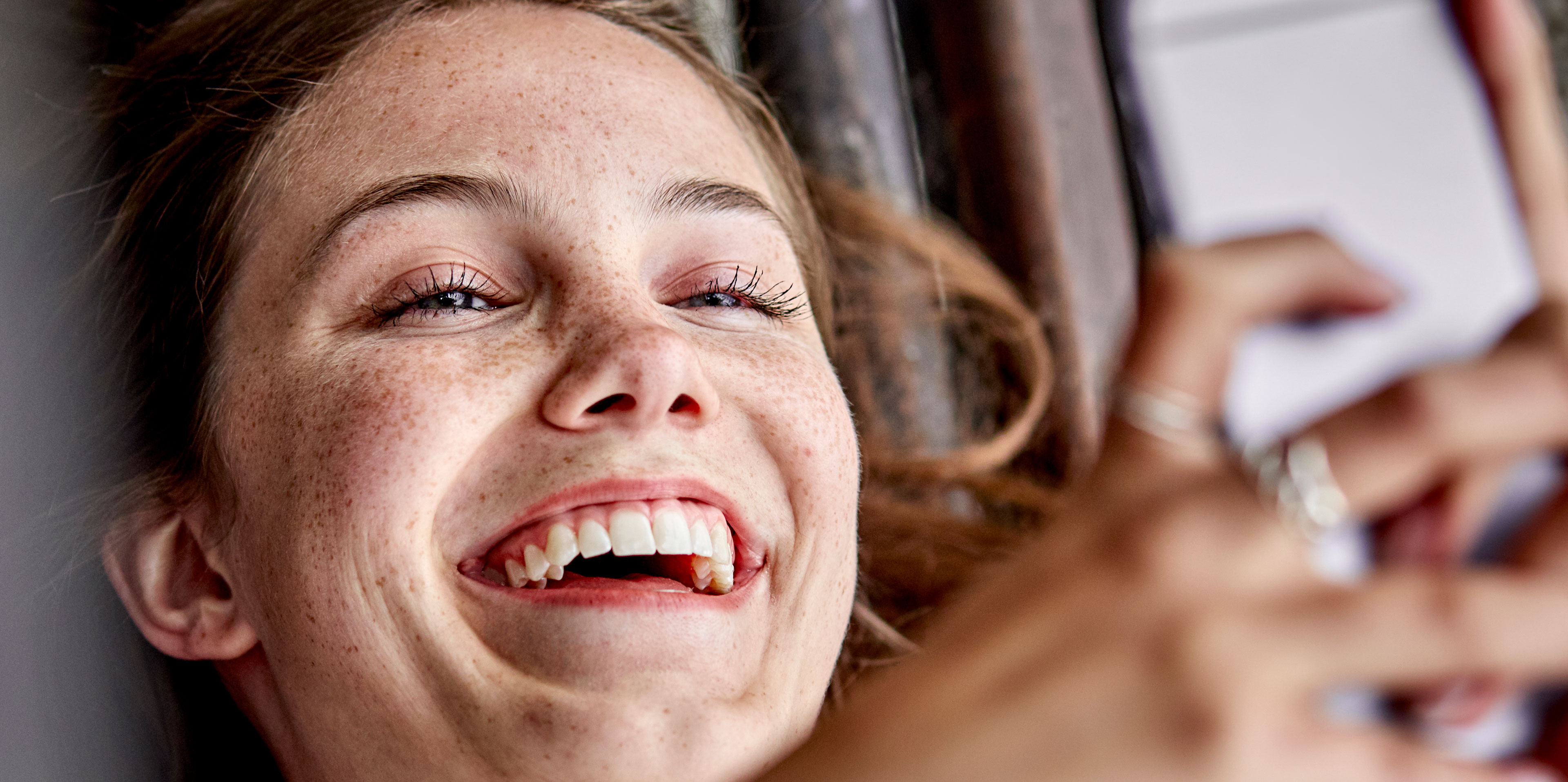 Een vrouw kijkt naar een telefoon in haar handen en glimlacht.