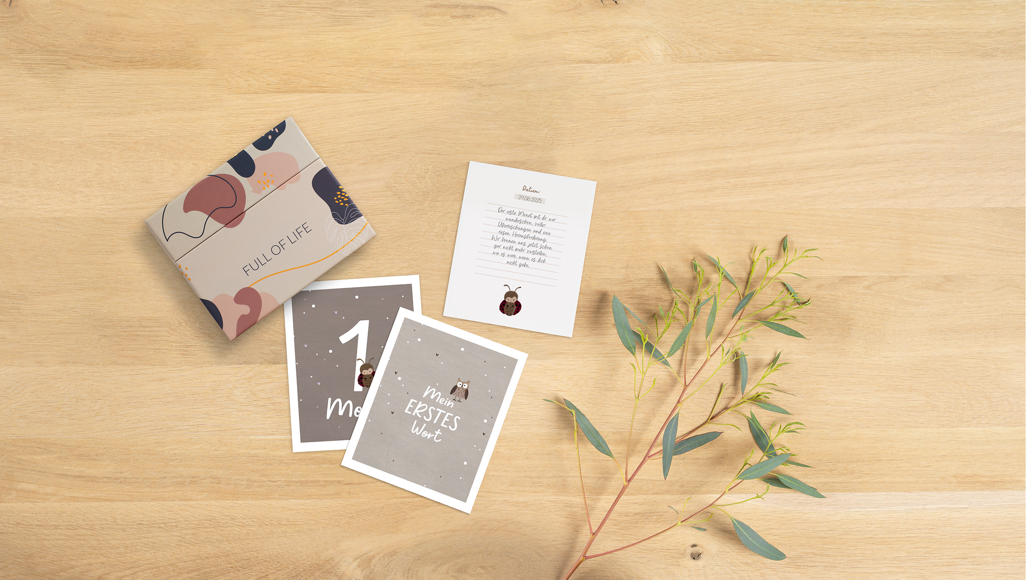 Drei Meilensteinkarten liegen auf einem Tisch neben einer schönen Aufbewahrungsbox mit modernem Design. Zwei der Karten zeigen die Vorderseite, jeweils mit einem Meilenstein. Die dritte Karte zeigt die Rückseite auf der handschriftlich Erinnerungen an einen Meilenstein festgehalten wurden.