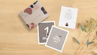Meilensteinkarten mit Tierdesign und Aufbewahrungsbox Drei Meilensteinkarten liegen auf einem Tisch neben einer schönen Aufbewahrungsbox mit modernem Design. Zwei der Karten zeigen die Vorderseite, jeweils mit einem Meilenstein. Die dritte Karte zeigt die Rückseite auf der handschriftlich Erinnerungen an einen Meilenstein festgehalten wurden.
