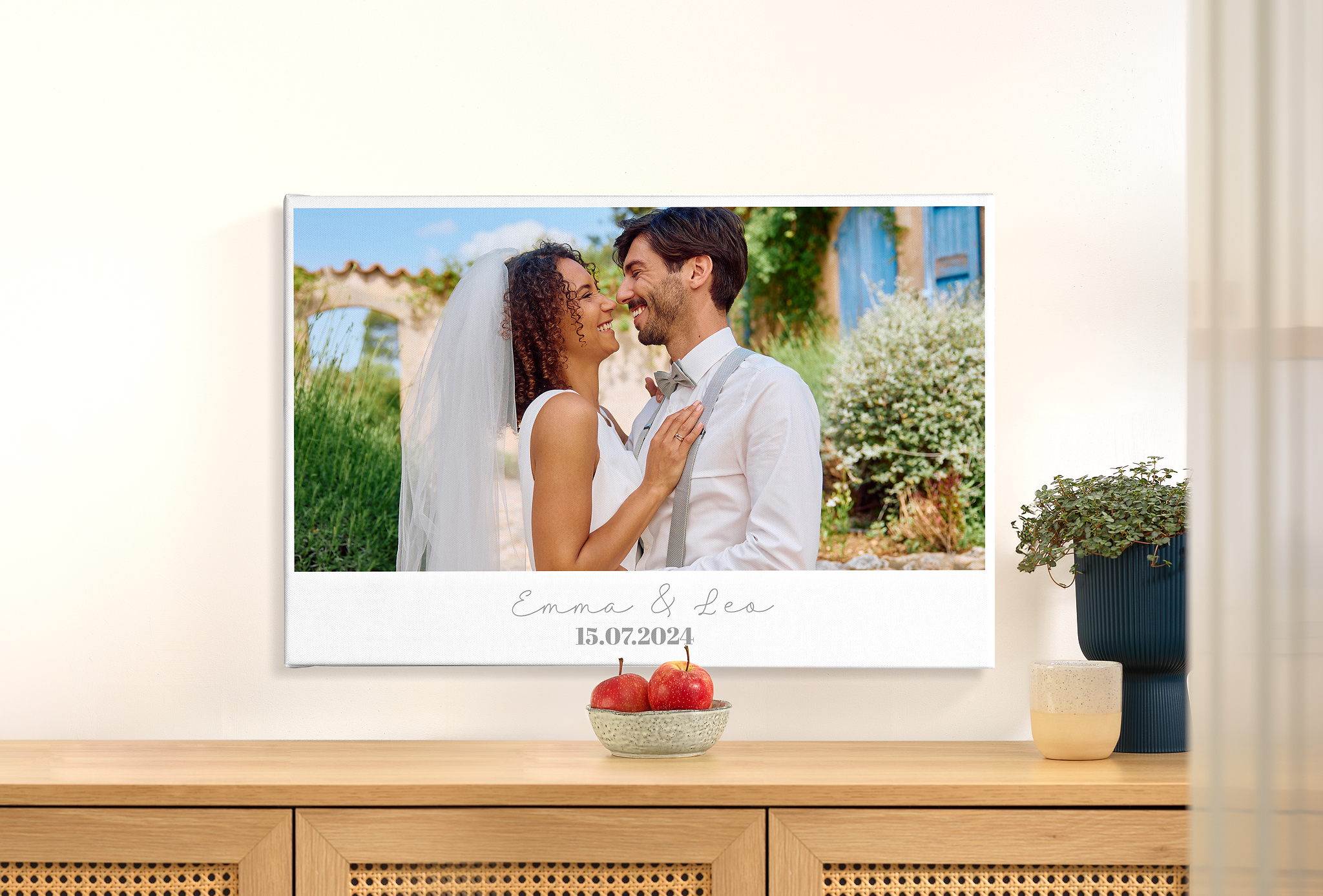 Eine Fotoleinwand hängt an einer Wand. Die Leinwand ist mit einem Hochzeitsfoto eines Paares sowie dem Wunschtext "Emma & Leo" - 15.07.2024" gestaltet.