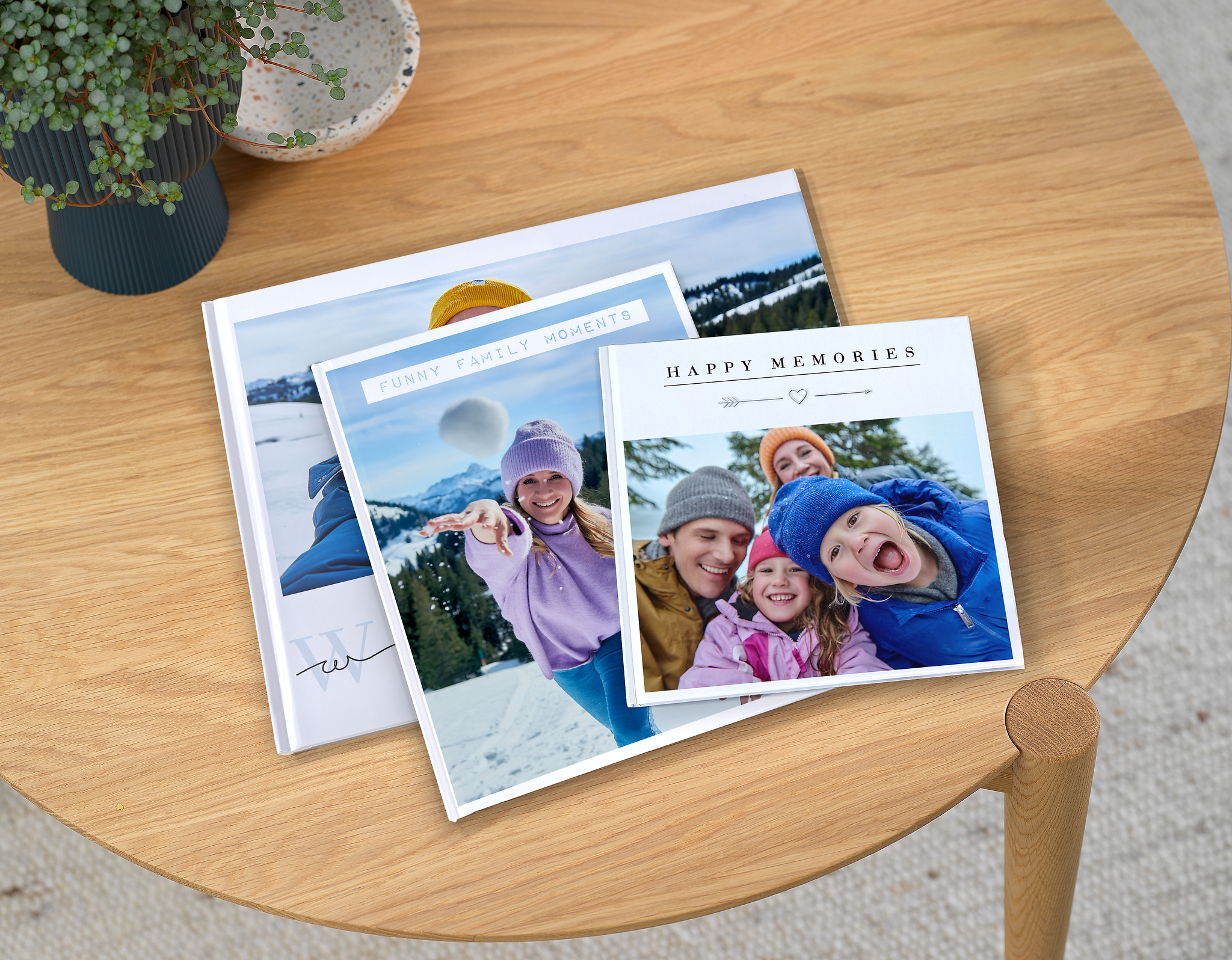 Pixum Fotobücher in drei verschiedenen Formaten mit Familienfotos im Schnee auf einem Tisch