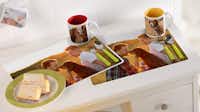 Placemat maken Bureautafel met daarop twee placemats en mokken met foto's.
