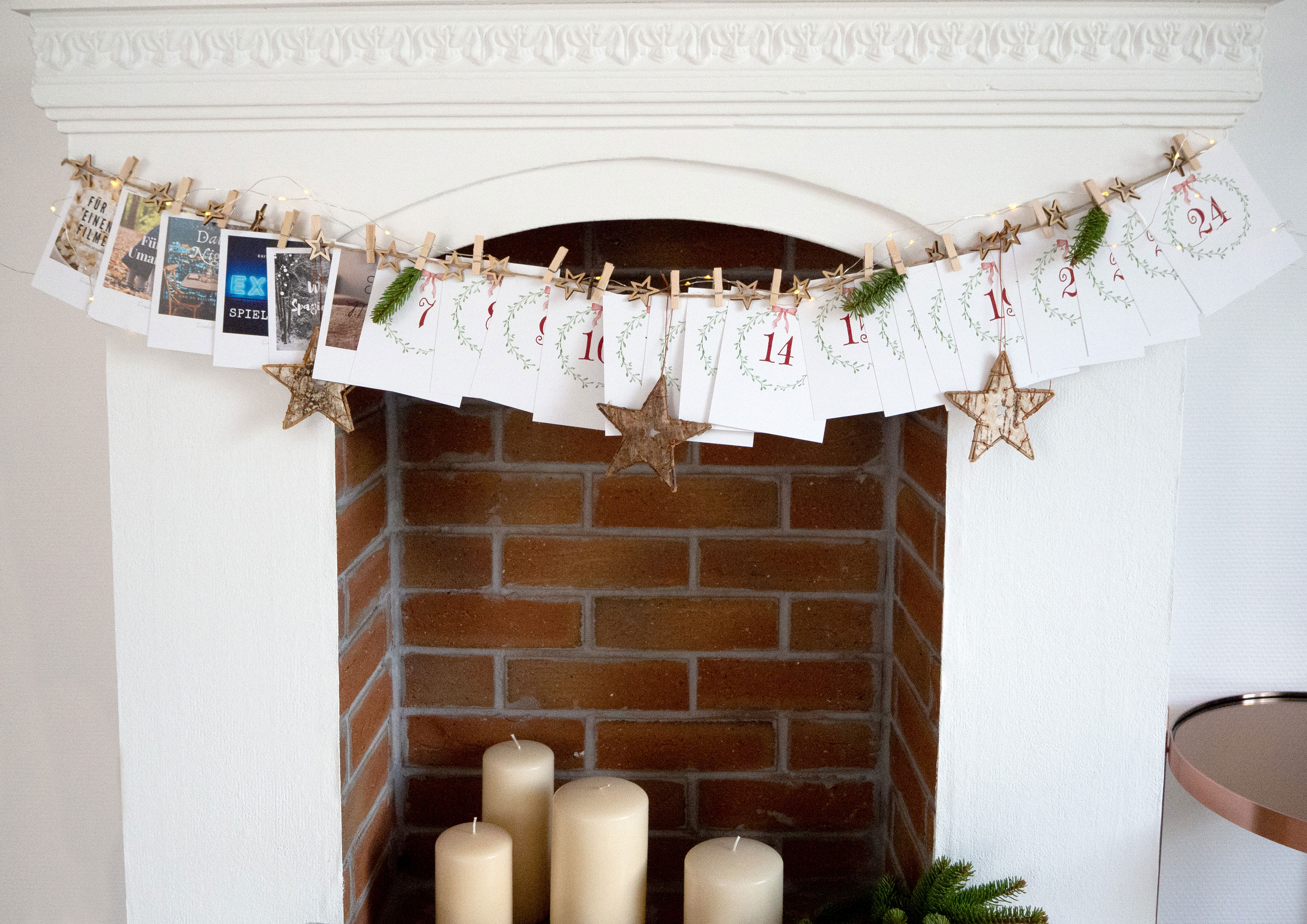 Ein Kamin mit einer Girlande aus nummerierten Retrofotos, die an einer Schnur mit Holzklammern aufgehängt sind und einen Foto-Adventskalender bilden.
