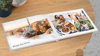 Reisefotobuch mit Fotos aus Barcelona Auf einem Tisch liegt ein aufgeklapptes Fotobuch, dass mit einem schönen Design sowie Reisefotos aus Barcelona gestaltet wurde. Auf den Reisefotos ist ein Pärchen zu sehen.