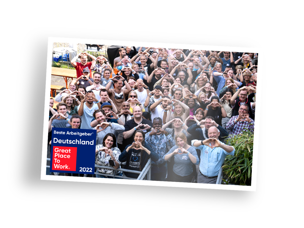 Fotoabzug, der viele Pixum Mitarbeiter zeigt, die mit den Händen ein Herz formen mit einem Great Place to Work Logo am linken Bildrand