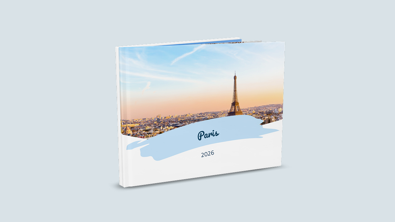 Ein aufgestelltes Reisefotobuch zeigt ein Cover mit dem Titel "Paris" und dem Untertitel "2026". Der Titel ist in blau hinterlegt. Das Cover zeigt ein Foto von Paris.