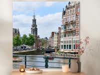 Canvas 100x100 cm bestellen Een canvas in het formaat 100x100 cm met een foto van Amsterdam hangt aan de muur.