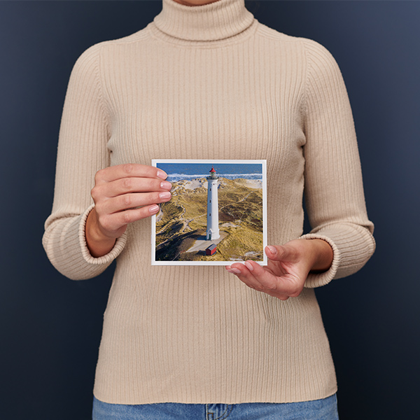 En kvinde holder en lille fotobog i kvadratiskformat med et landskab i sine hænder