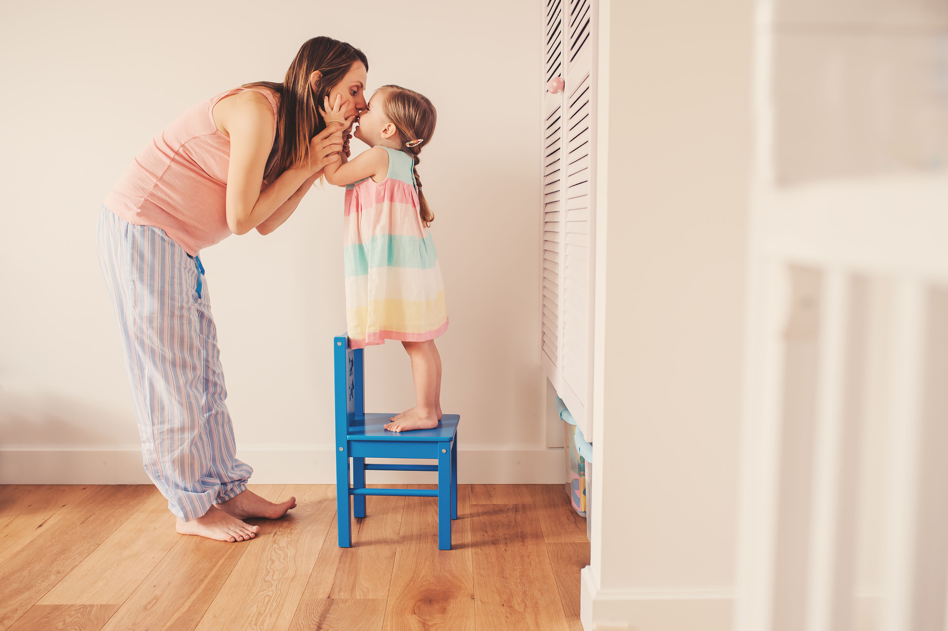 Een moeder kust haar dochter die op een stoel staat.