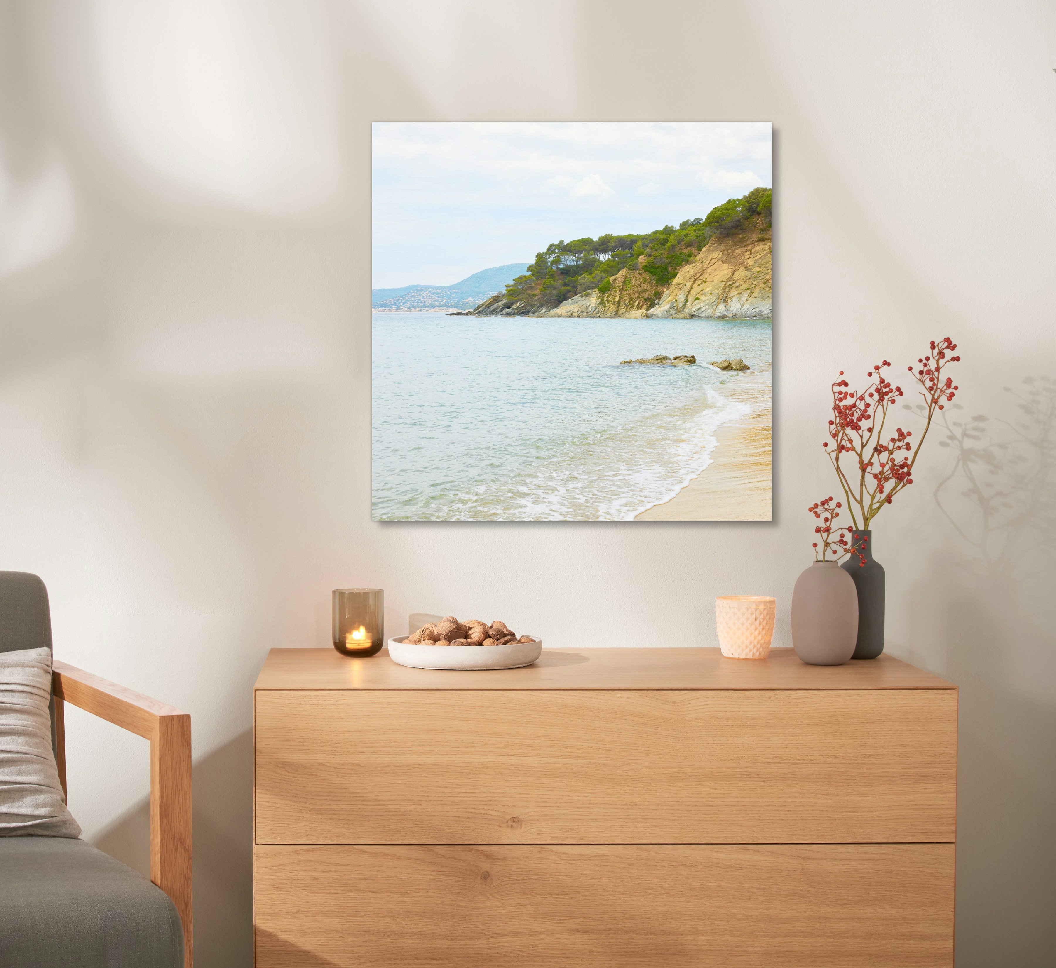 Ein Wandbild aus Holz mit einem Urlaubsfoto hängt an einer Wand, über einer Kommode. 