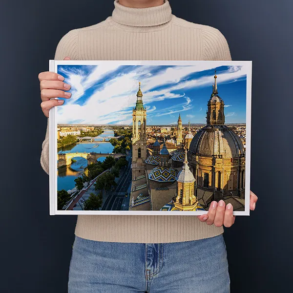Persoon houdt een fotoboek vast met daarop een lavendelveld bij zonsondergang met een boerderij en boom op de achtergrond.