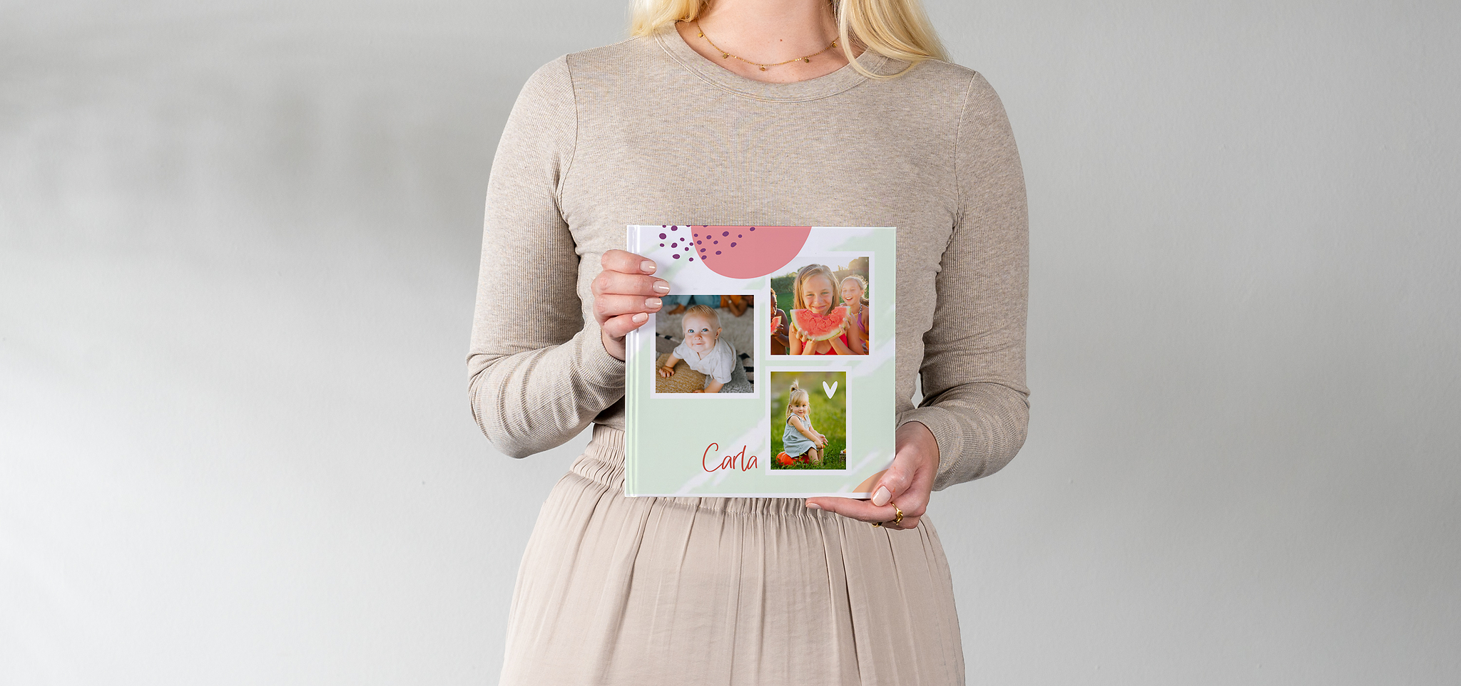 Ein als Babyalbum gestaltetes Fotobuch wird von einer Frau gehalten. Das Cover ist bunt mit mehreren Fotos gestaltet.