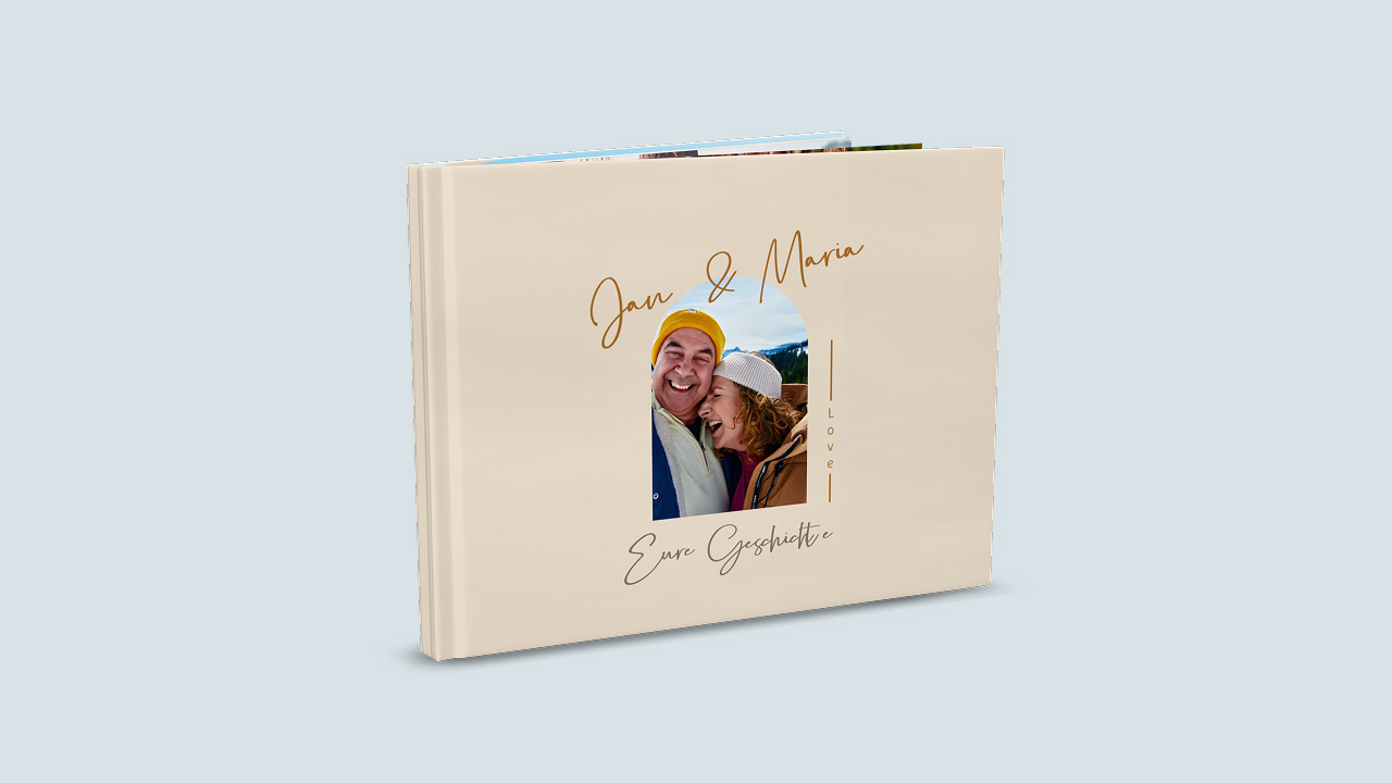 Ein aufgestelltes Fotobuch mit einem Fotobuch-Cover gestaltet zum Thema Liebe. Im Zentrum befindet sich das Foto eines Pärchens. darüber stehen die Namen "Jan & Maria". Unter dem Foto steht der Titel "Eure Geschichte". Das Fotobuch ist hellbraun.