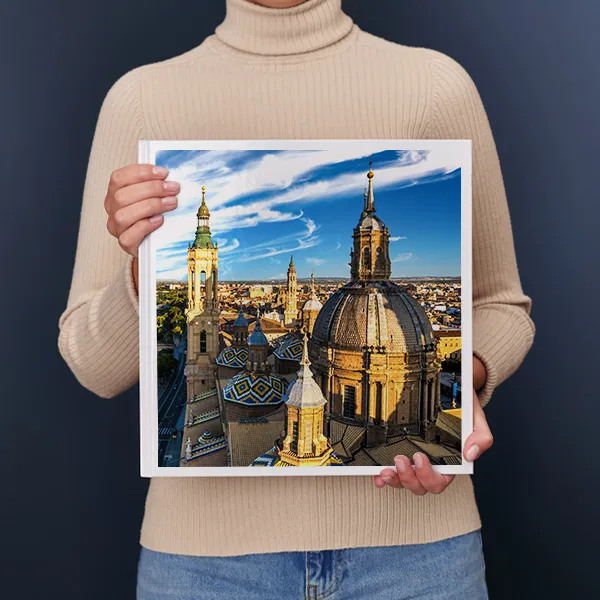 Een persoon houdt een fotoboek vast met daarop een lavendelveld bij zonsondergang met een eenzame boom en huis op de achtergrond.