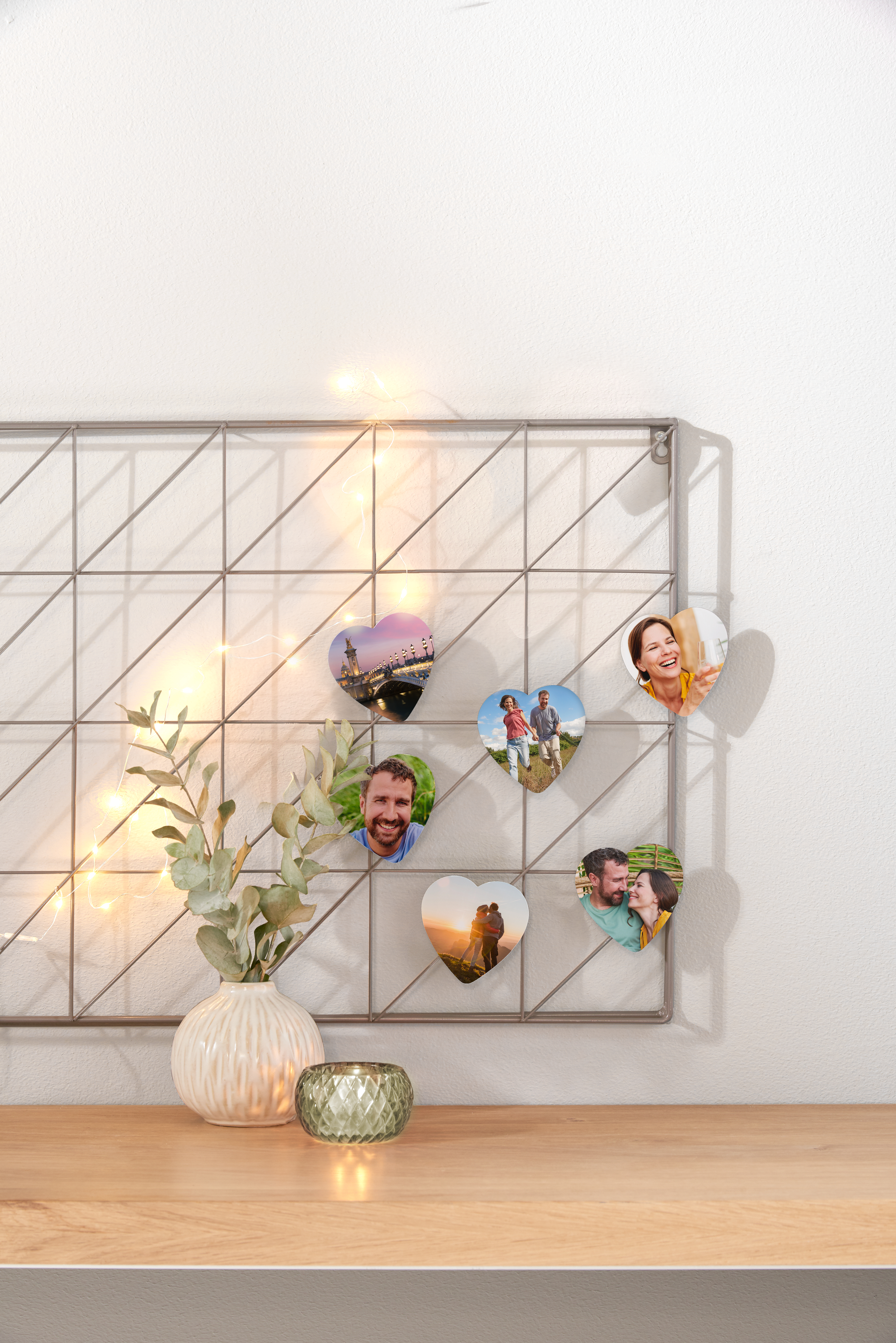 Ein Wandgitter mit Fotomagneten in Herzform und Lichterketten. Die Fotos zeigen persönliche und emotionale Momente.