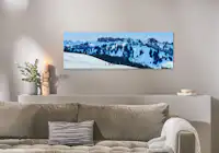 Fotoleinwand im Format 150x50 cm Eine Fotoleinwand im Format 150x50 cm hängt über einem Sofa und zeigt ein Bild von einer winterlichen Berglandschaft.