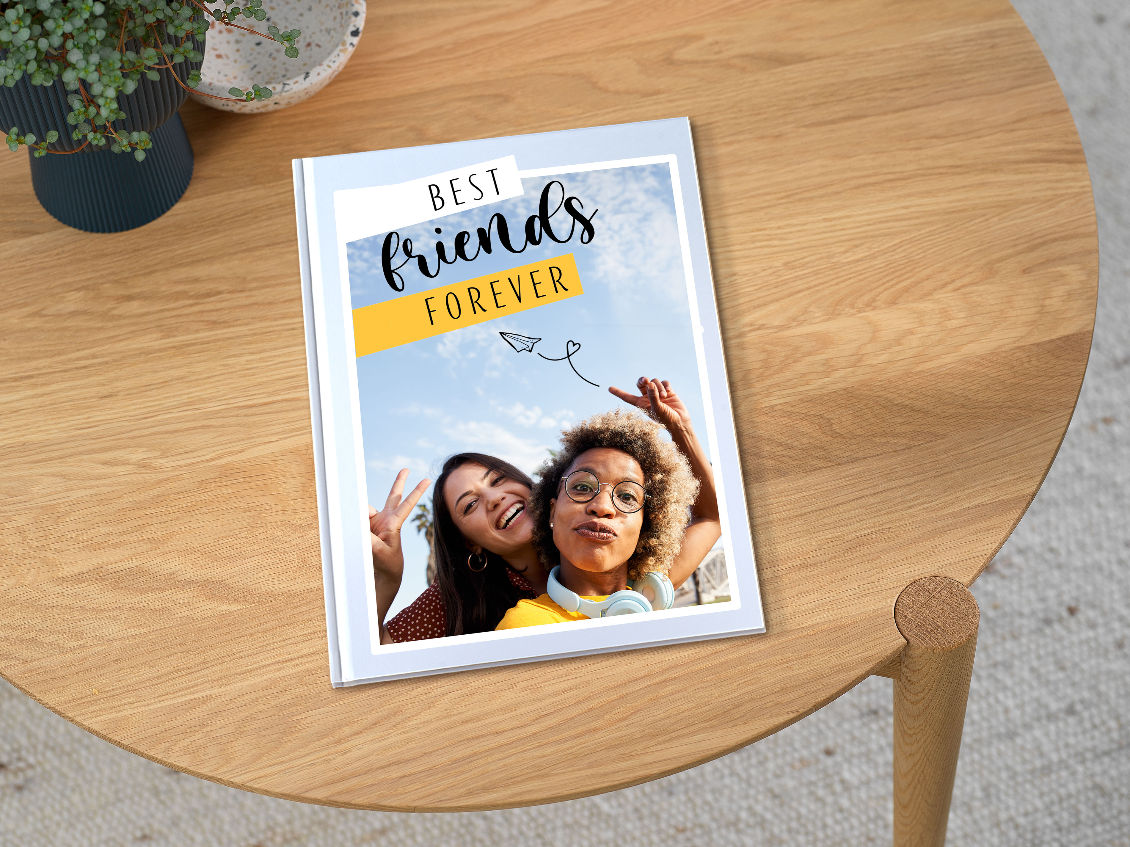 Ein Pixum Fotobuch im großen Hochformat, welches auf einem Tisch liegt. Auf dem Cover steht "Best Friends Forever".