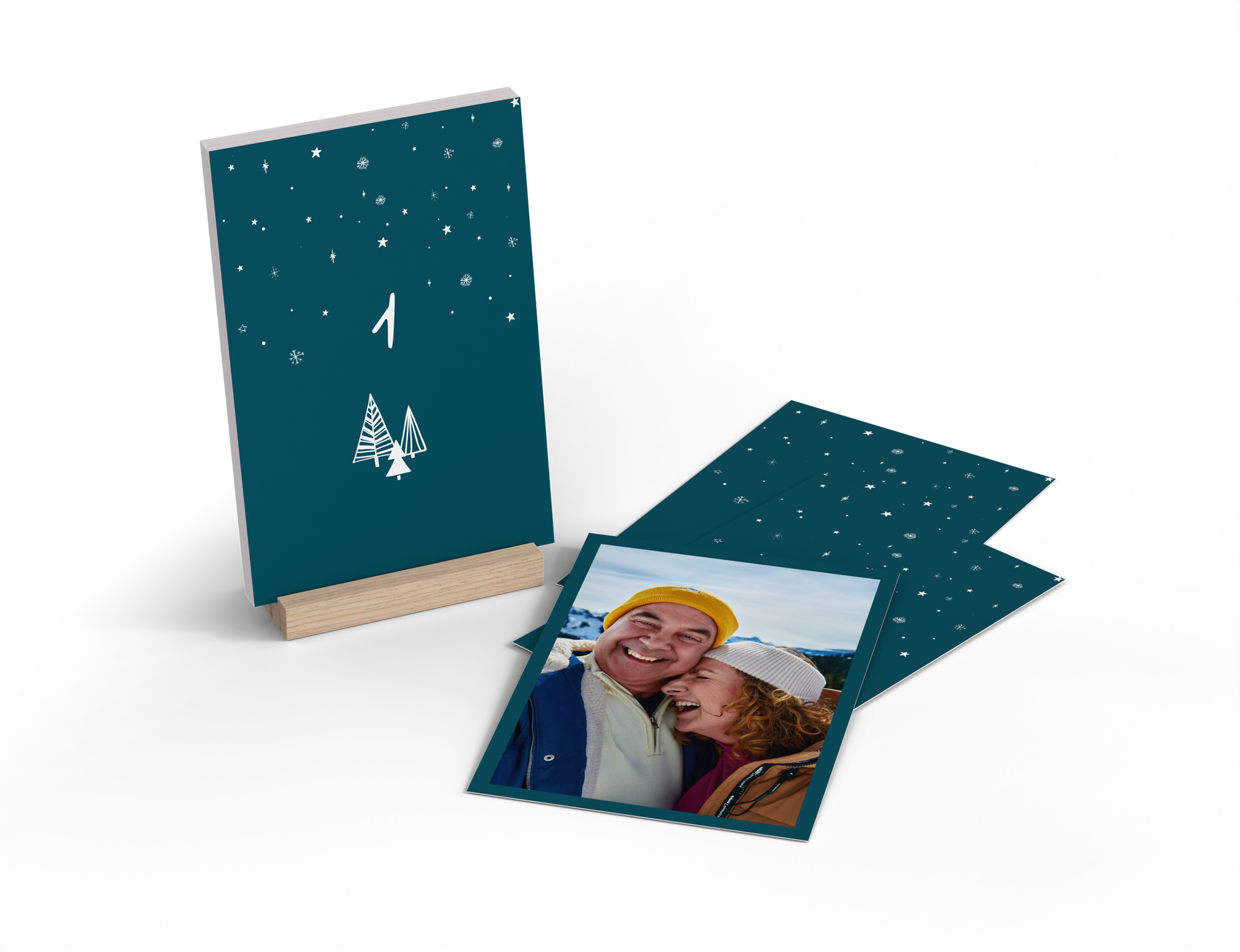 Calendario de Adviento de mesa con 24 tarjetas fotográficas personalizadas. El reverso está decorado con un diseño de Adviento en azul oscuro. En el centro de la tarjeta aparece el número correspondiente del 1 al 24, sobre él cae nieve y debajo hay abetos.