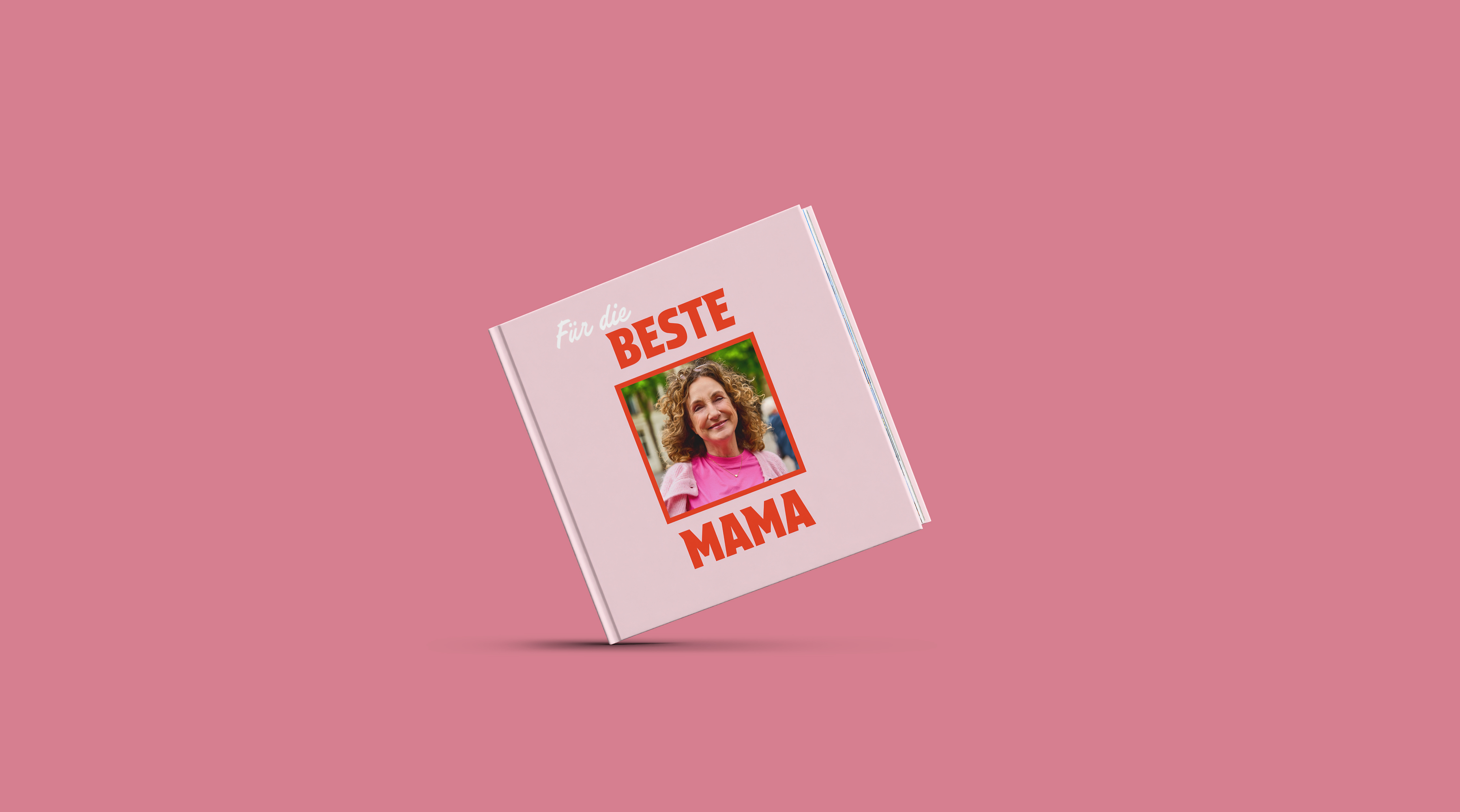 Eine Person hält ein Fotobuch in der Hand. Dieses ist mit rosafarbenen Elementen zum Muttertag gestaltet.