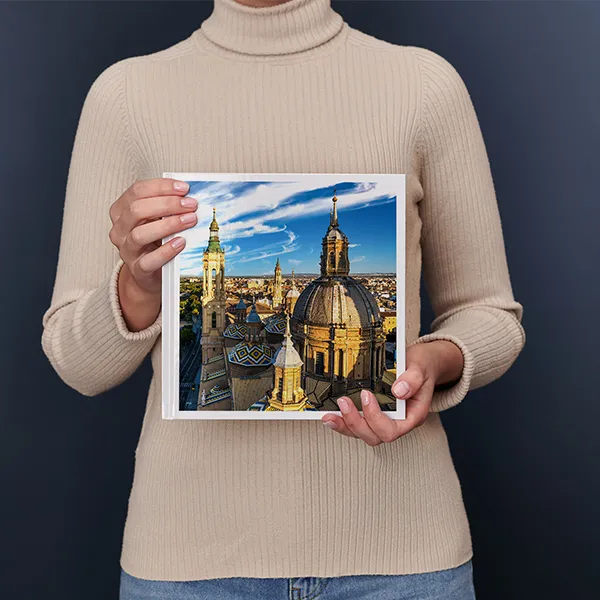 Persoon houdt een fotoboek vast met daarop een lavendelveld met een huis en boom tijdens zonsondergang.