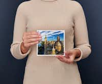 Fotoboek klein vierkant Een persoon in een beige trui houdt een fotoboek vast met daarop een lavendelveld met een boom en een huis in de achtergrond.