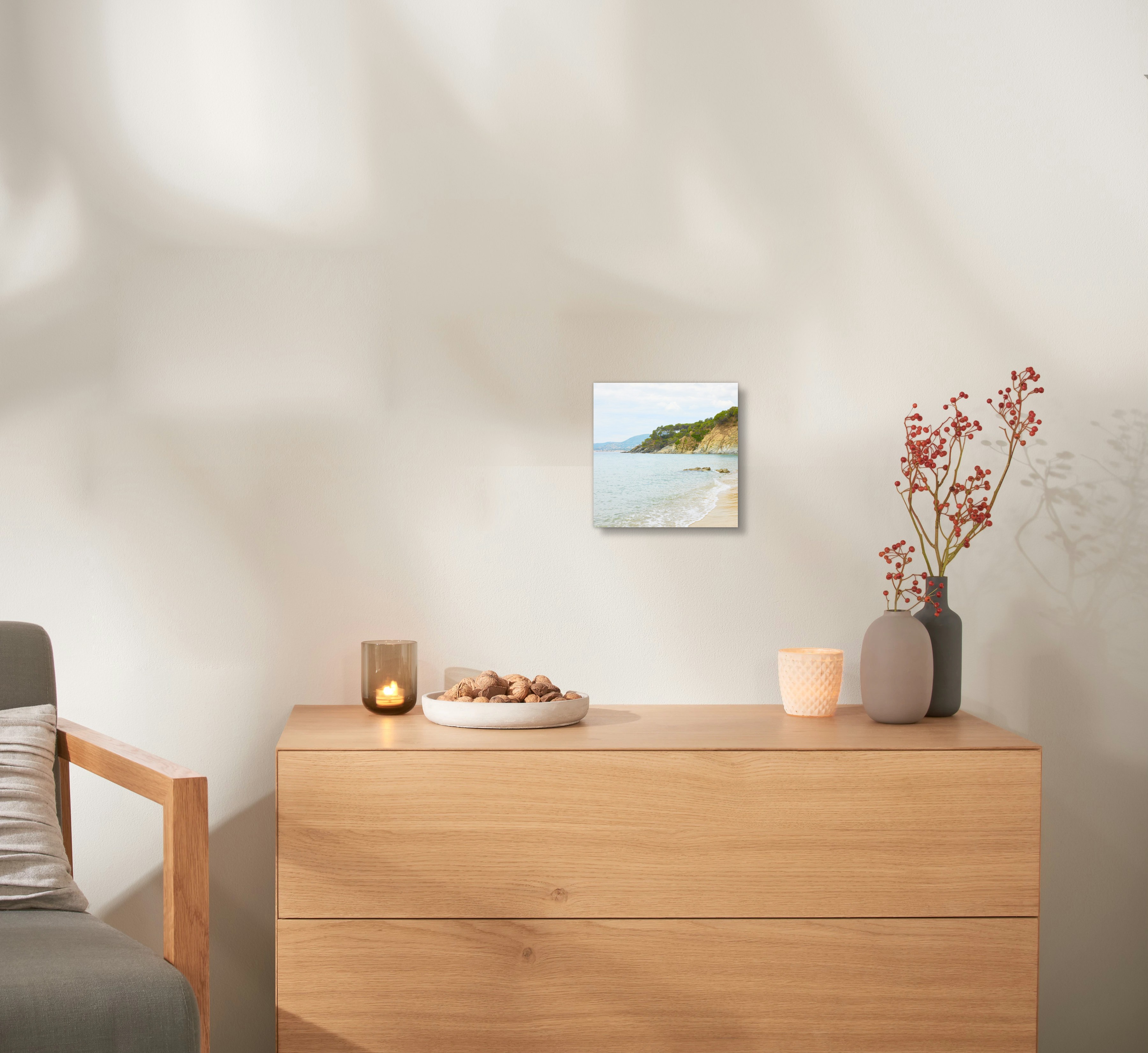 Ein Wandbild aus Holz mit einem Urlaubsfoto hängt an einer Wand, über einer Kommode. 