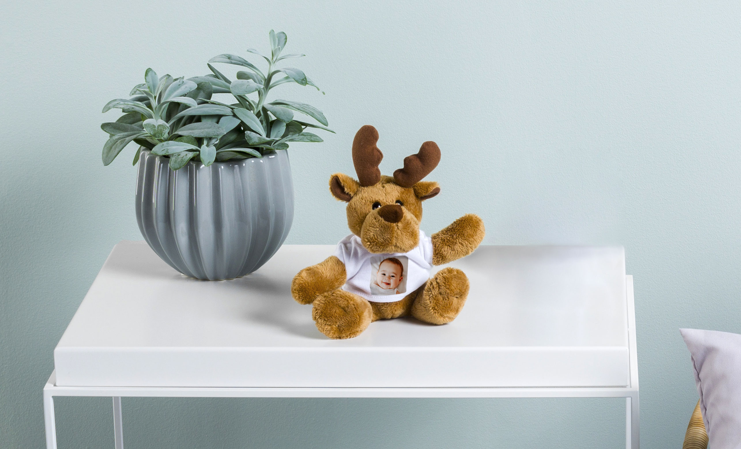 Een knuffel in de vorm van een rendier met een T-shirt aan met daarop een foto van een baby.