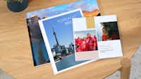 Fotobücher in der Pixum App gestalten Drei Fotobücher mit kreativen Urlaubsfotos liegen übereinander gestapelt auf einem Tisch. Sie sind unterschiedlich gross und bunt gestaltet.