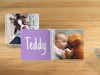Álbum de fotos para bebé Pixum con una foto de bebé y osito de peluche sobre una mesa de madera