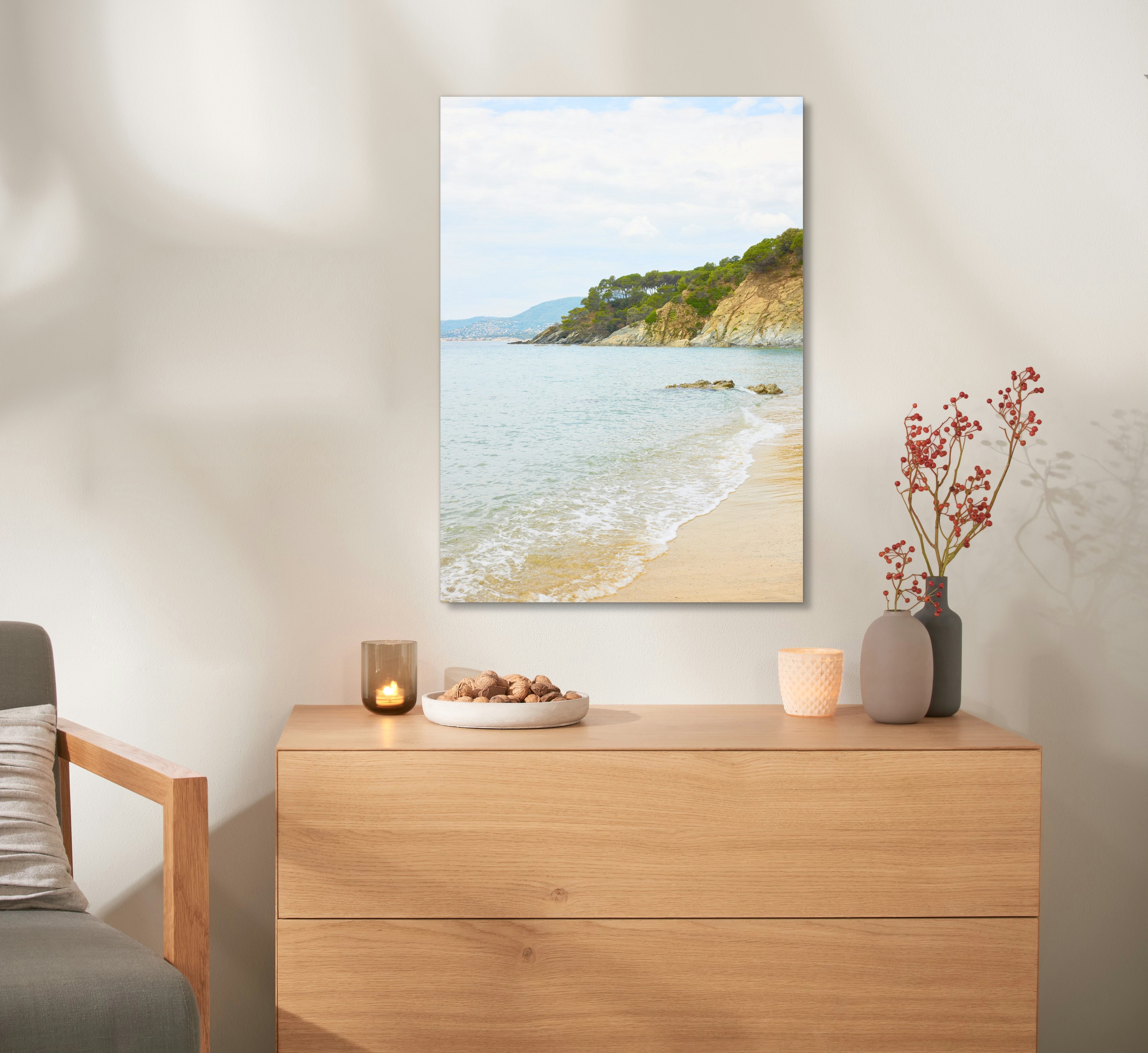 Ein Wandbild aus Holz mit einem Urlaubsfoto hängt an einer Wand, über einer Kommode. 